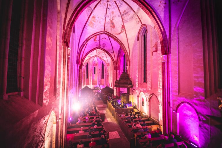 Interieur van een kerk met kleurrijke verlichting en een lange zichtlijn naar het altaar.
