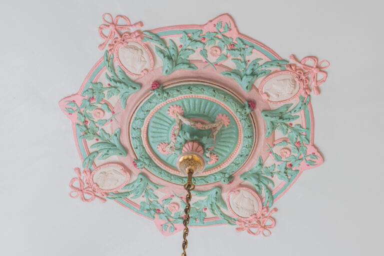 Decoratief plafondornament in pastelkleuren met bloemen- en gezichtenmotieven.