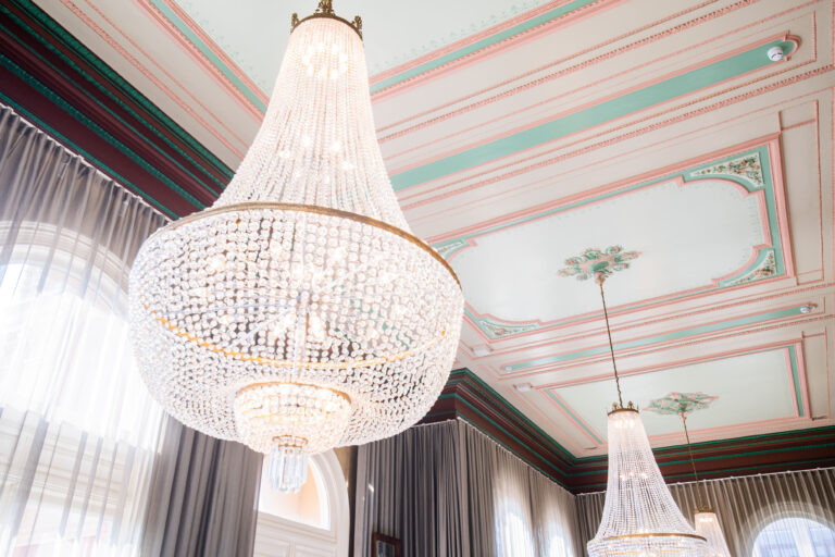 Twee elegante kristallen kroonluchters hangen aan het plafond met gekleurde details.