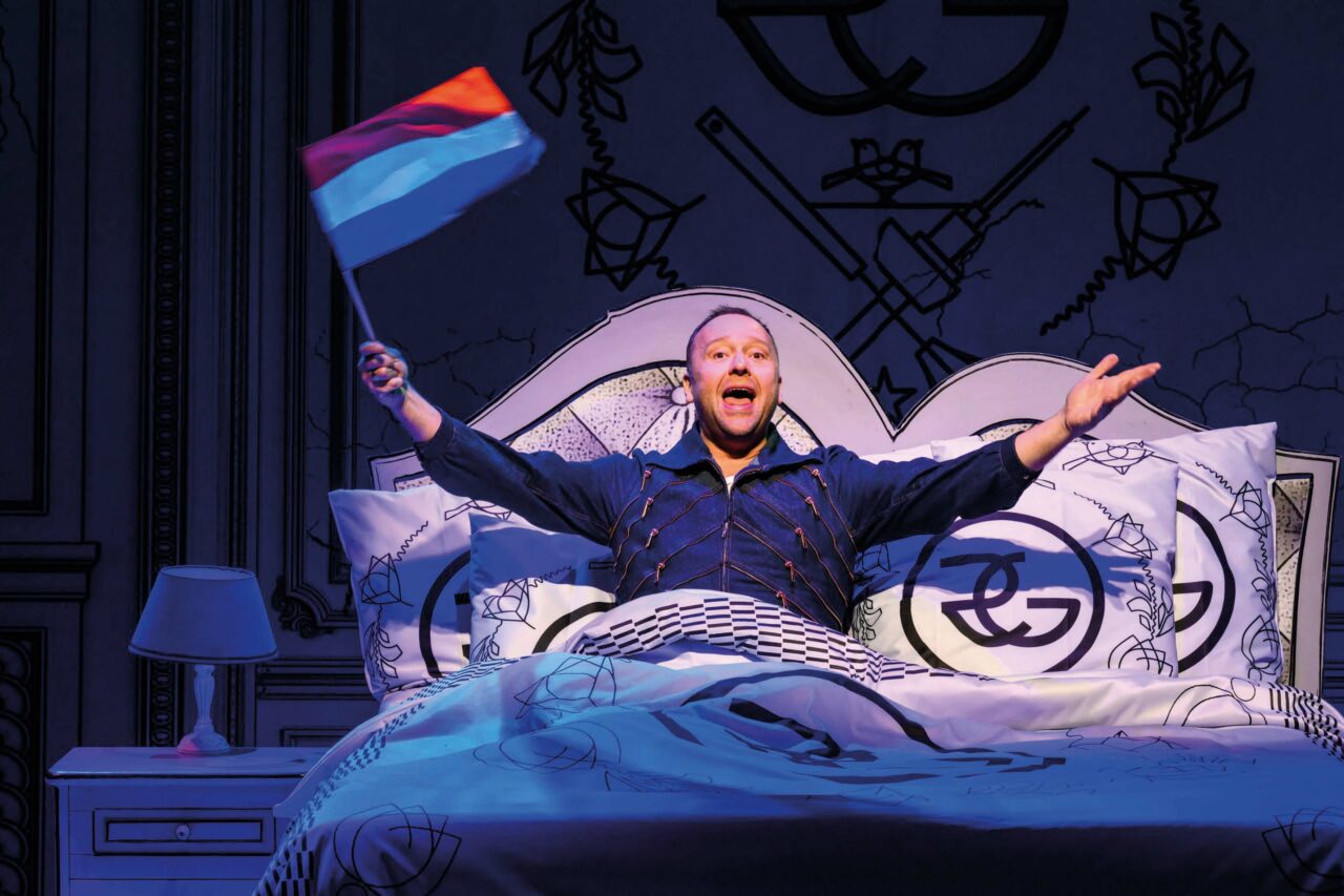 Een persoon ligt op een bed en houdt een vlag omhoog in een feestelijke houding.