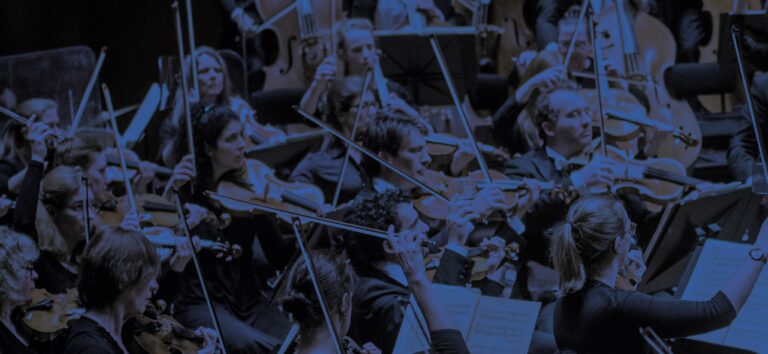 Een groep muzikanten van een symfonieorkest bespeelt hun instrumenten in een donkere setting.