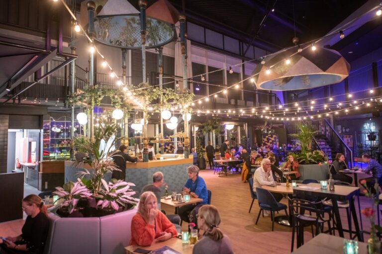 Gezellig restaurant met etende mensen onder verlichte lichtsnoeren met lampjes.