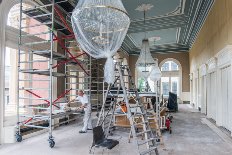 Verbouwing in het foyer van de Stadsschouwburg Groningen. Er staan allemaal steigers en ladders en een schilder die de ruimte aan het verven is.