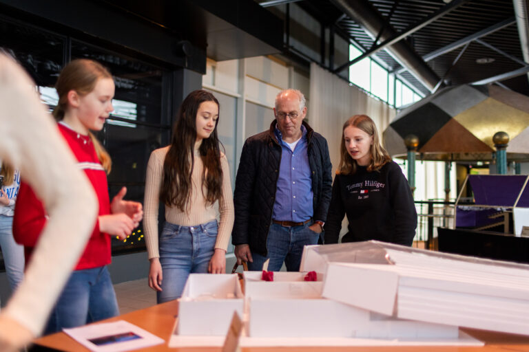 Een groep mensen bekijkt een model op een tafel in een moderne omgeving.