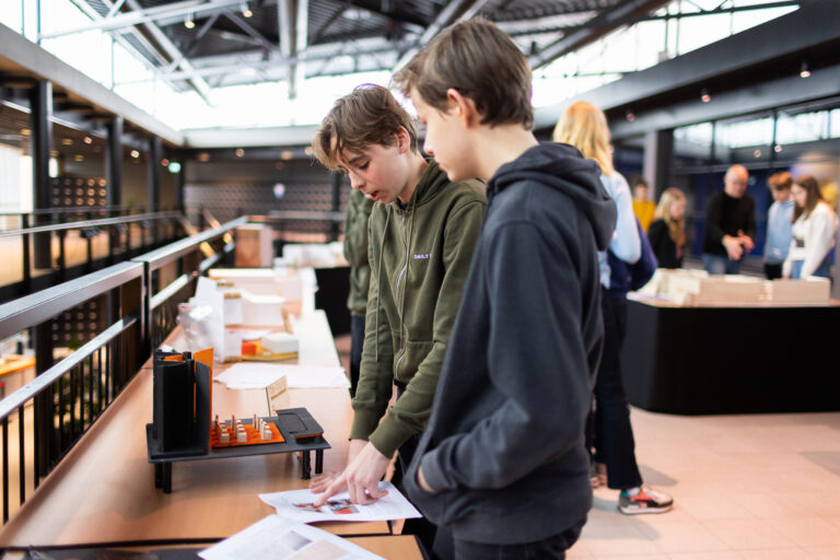 Twee tieners bekijken op een tafel documenten en affiches in een moderne ruimte.