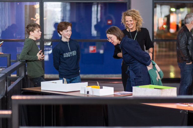 Een groep mensen kijkt en interacteert met modellen op een tafel in een moderne ruimte.