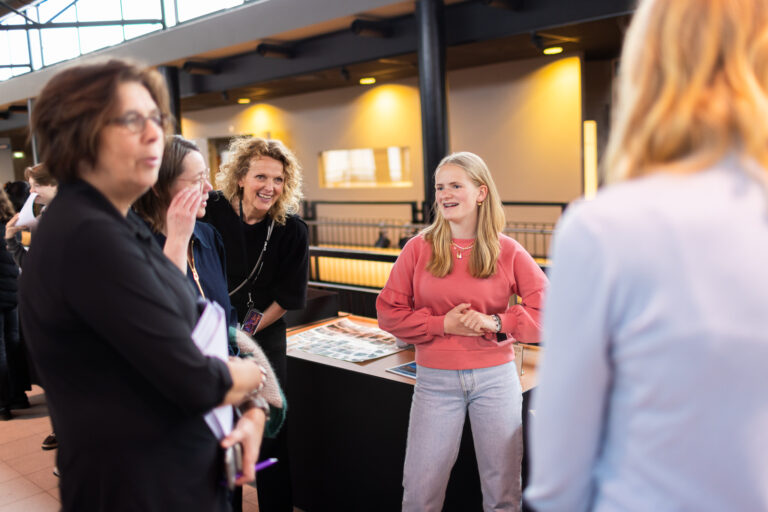 Een groep mensen staat samen te lachen en te praten in een heldere, moderne ruimte.