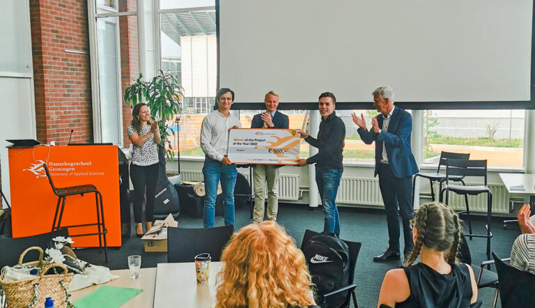 Prijswinnaars CrossWise met project Open Podium houden cheque 500 euro vast voor publiekp groot scherm met publiek