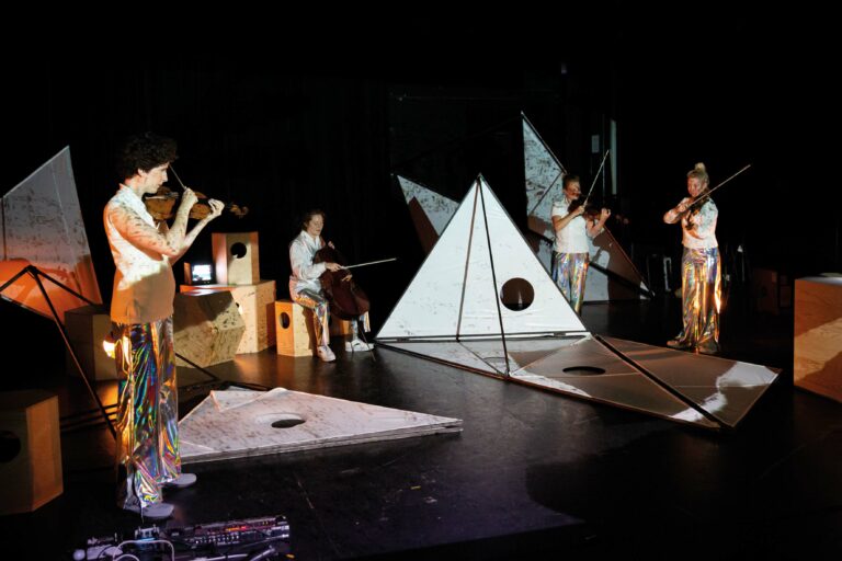 Een groep muzikanten speelt op het podium, omringd door verschillende geometrische sculpturen en projecties.