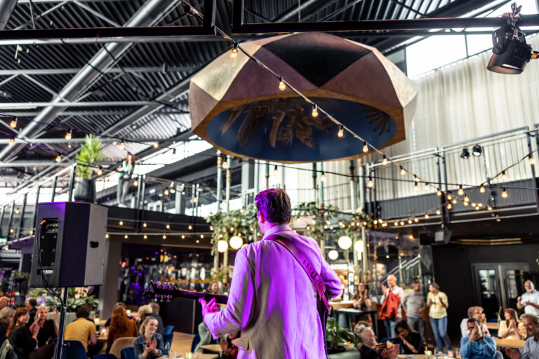 Artiest met gitaar op het open podium in het Café van De Oosterpoort.