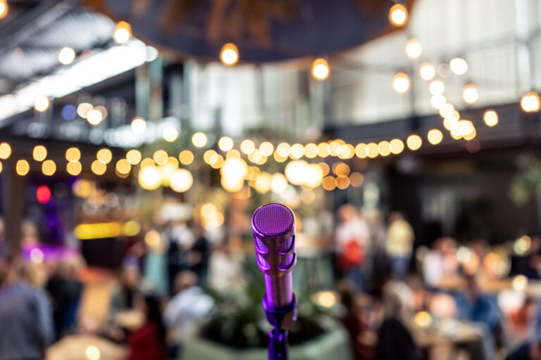 Ingezoomd op een paarse microfoon met een blurry Café op de achtergrond.