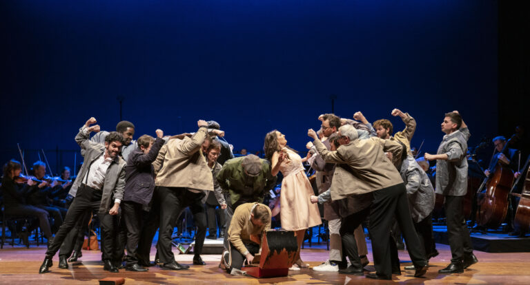 Een toneelstuk waarin een vrouw in een lichte jurk omringd wordt door een groep mannen in jassen, die zich theatrale gebaren maken.