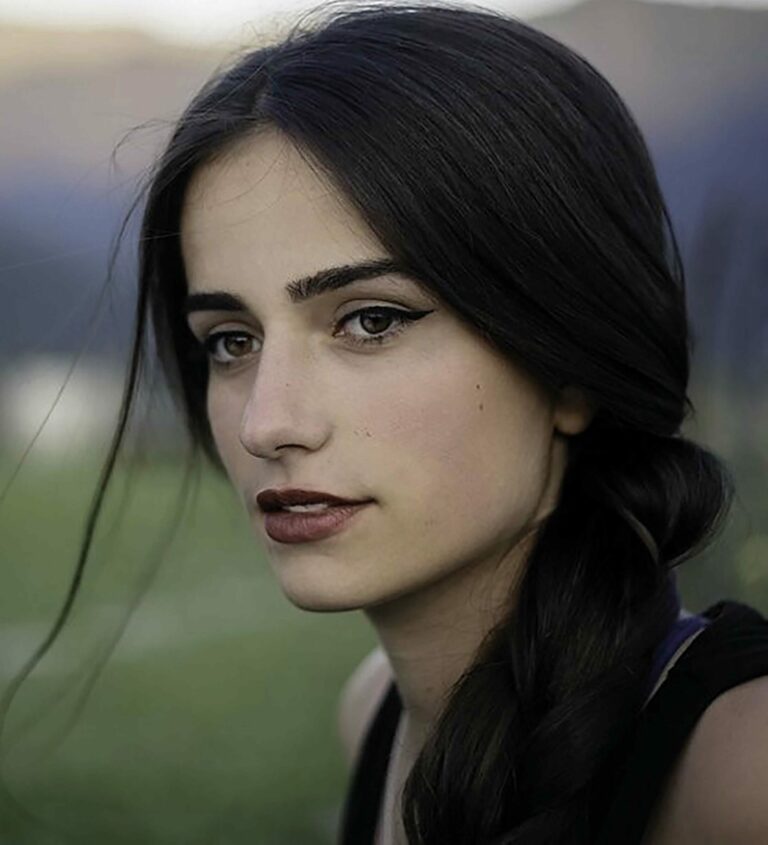 Portret van een vrouw met lang, zwart haar en een lichte glimlach, tegen een groene achtergrond.