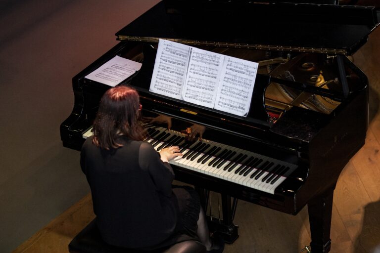 Een vrouw speelt een stuk op een piano met bladmuziek voor zich.