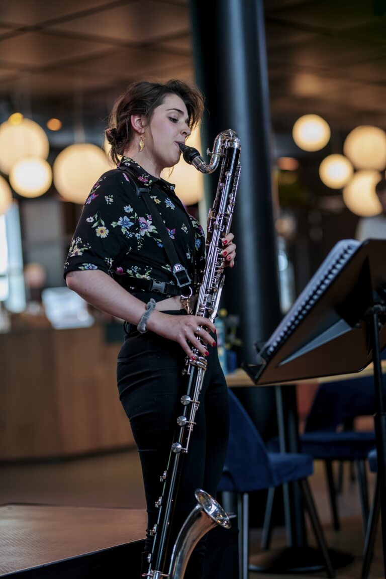 Een muzikante speelt een hobo op een podium, omringd door sfeervolle verlichting.