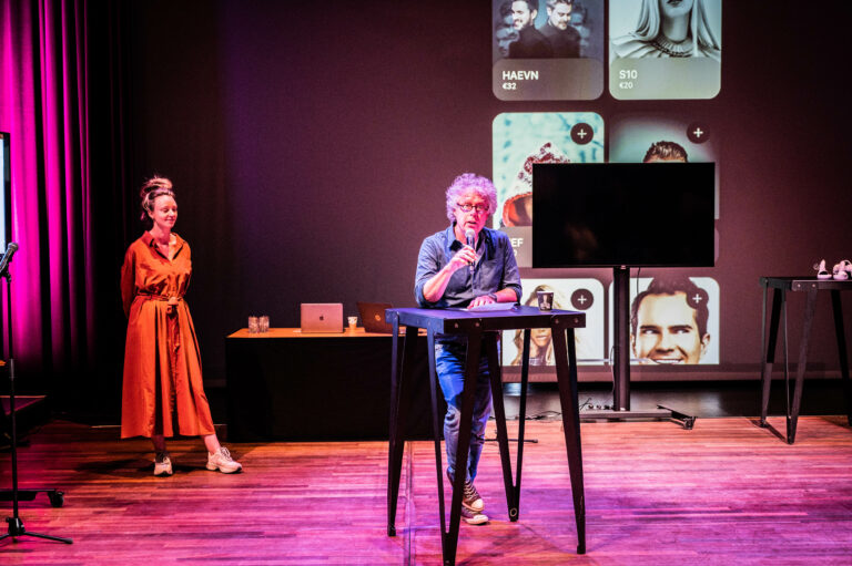 Presentator van New Technology zit op een hoge kruk en geeft praatje.