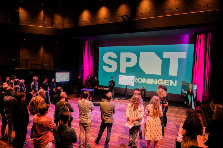 Deelnemers staan op de vloer van de kleine zaal tijdens event.