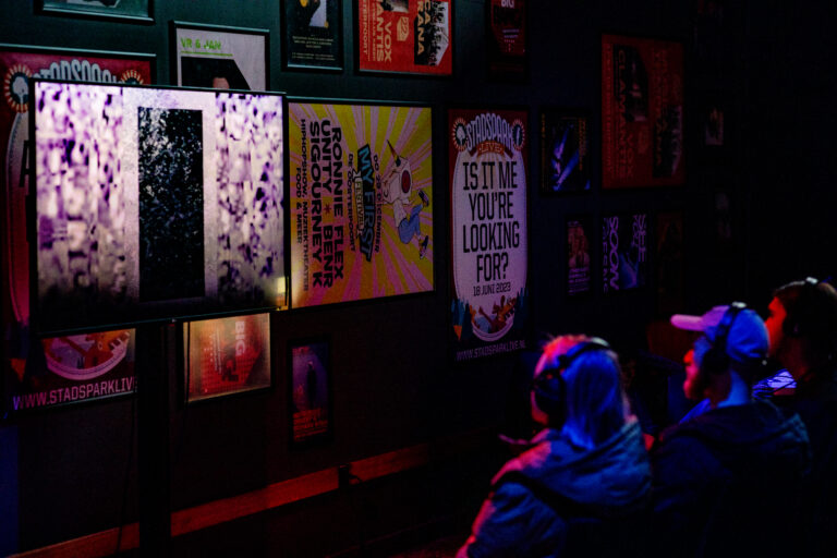 Mensen die met een koptelefoon op kijken naar een muur met posters.