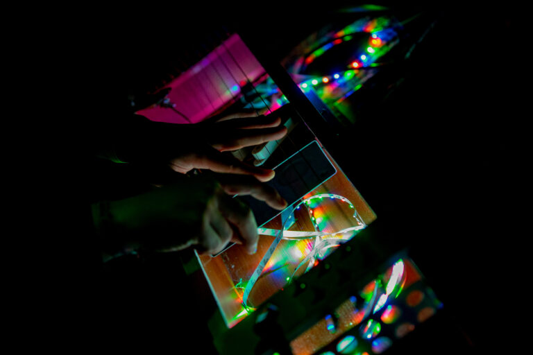 Twee handen met daar omheen draadjes met regenboog verlichting.