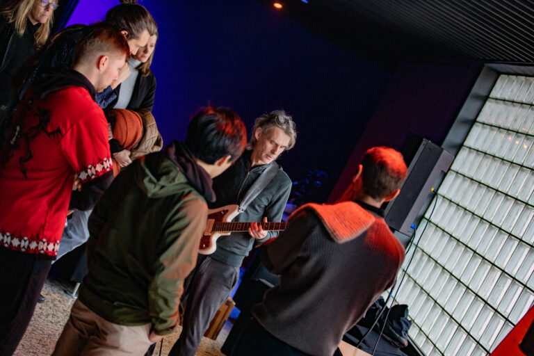 Groepje mensen om een man heen die gitaar speelt.