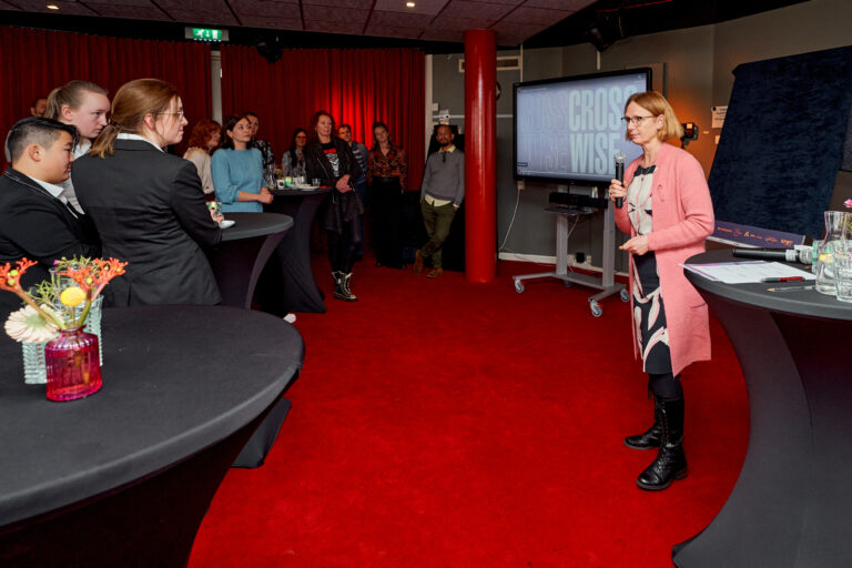 Een groep mensen in een moderne ruimte, waarbij een vrouw in roze een presentatie geeft voor een scherm.