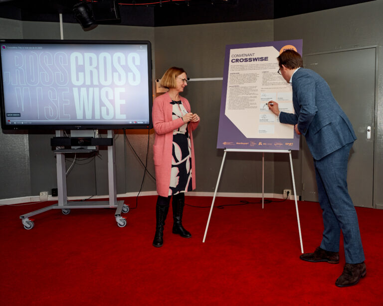 Twee mensen staan in een studio; de ene schrijft op een bord terwijl de andere toekijkt.