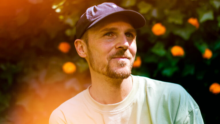 Portret van een man met een hoed, staande voor een groene achtergrond met oranje details.