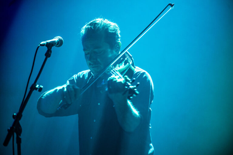 Een muzikant speelt viool onder een blauwe verlichting op een podium.