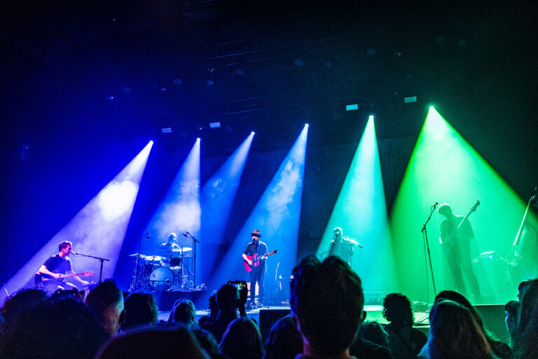 Een live concert met muzikanten op het podium en kleurrijke lichten in verschillende tinten.