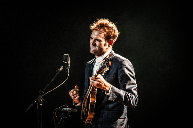 Een muzikant speelt op een mandoline voor een microfoon met een donkere achtergrond.
