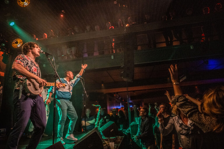 Een muzikant optredend op het podium met een enthousiast publiek dat hun handen in de lucht steekt.