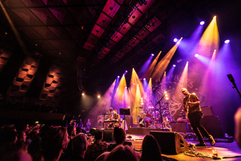 Een band optredend op een podium met kleurrijke verlichting en een enthousiast publiek.