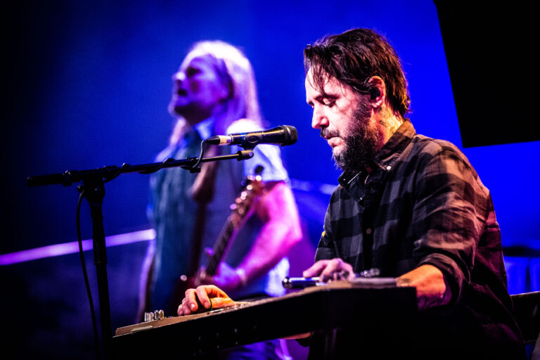 Een muzikant speelt op een keyboard terwijl een andere muzikant op de achtergrond zingt.