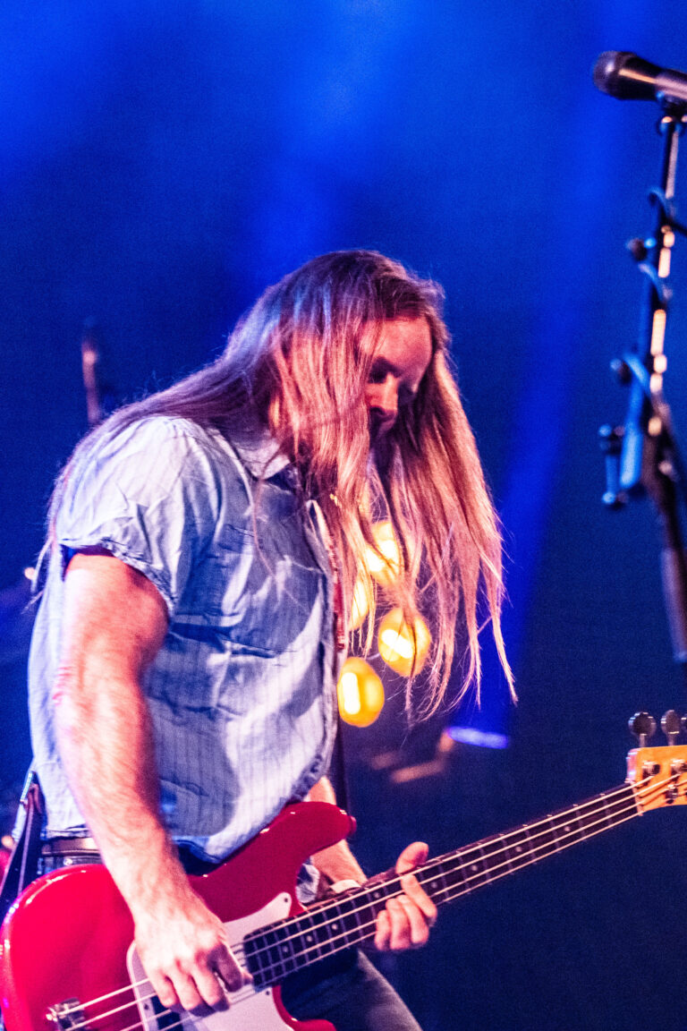 Een muzikant met lang haar speelt op een elektrische basgitaar tijdens een optreden.