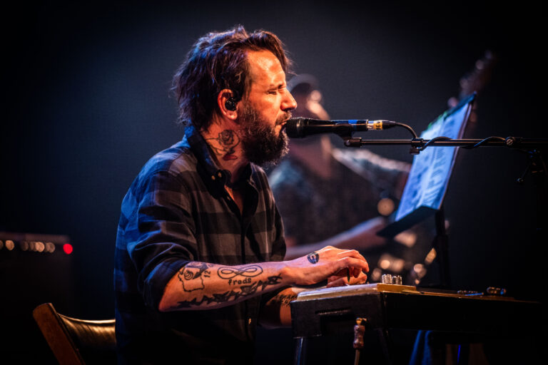 Een muzikant speelt een instrument terwijl hij zingt en een microfoon gebruikt op het podium.