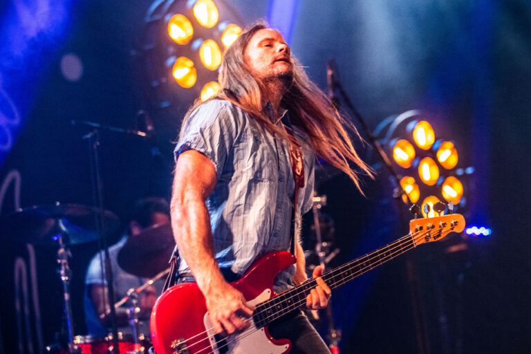 Een muzikant speelt gepassioneerd basgitaar op een podium, omringd door felle lichten.
