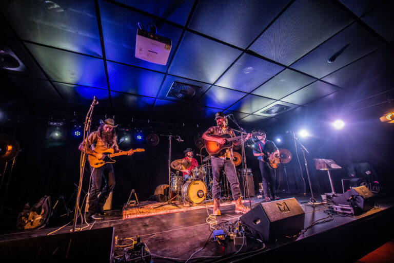 Een band speelt live muziek op een podium verlicht met blauwe en witte lichten.