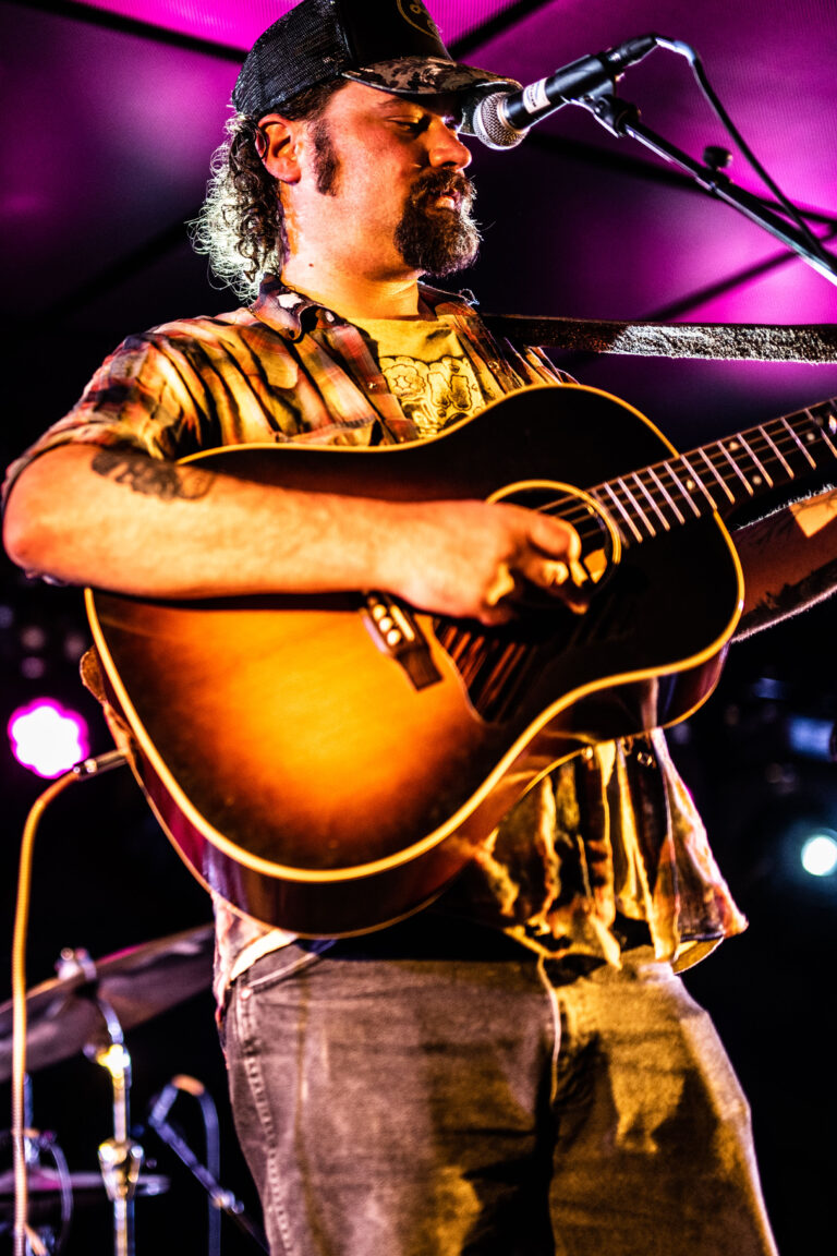 Een muzikant speelt gitaar op een podium met kleurrijke verlichting.