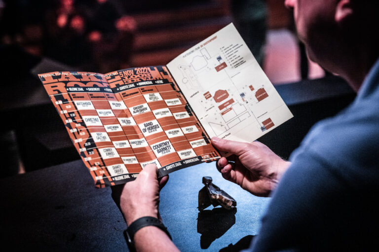 Iemand houdt een open menukaart vast met verschillende gerechten en prijzen in een restaurantsetting.