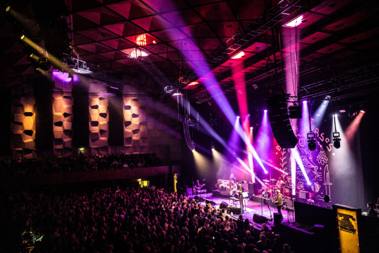 Een druk concert met kleurrijke verlichting en een enthousiaste menigte in de zaal.
