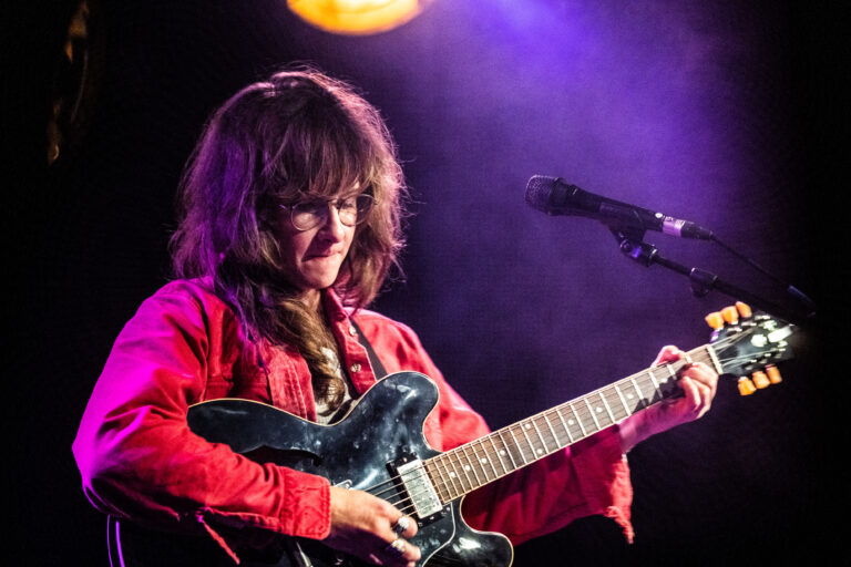 Een muzikant speelt gitaar op een podium met kleurrijke verlichting.