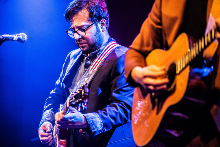 Een muzikant speelt gitaar op een podium met kleurige verlichting.