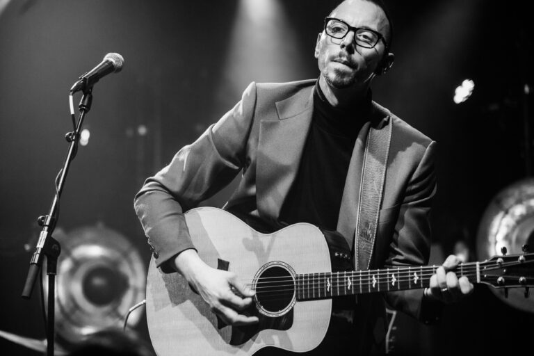 Een muzikant in een stijlvolle outfit speelt gitaar op het podium.