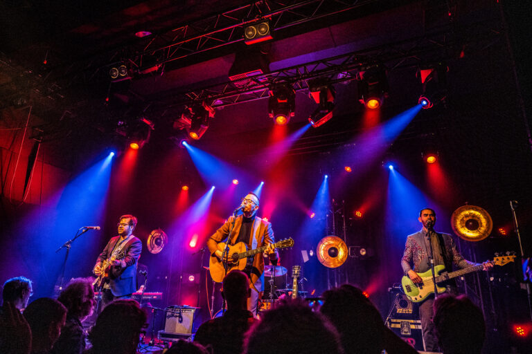 Een band speelt live op het podium met kleurrijke verlichting.