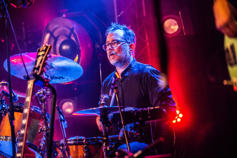 Een drummer die geconcentreerd speelt op een podium met kleurrijke verlichting.