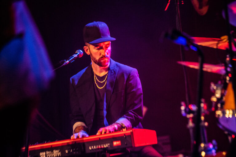 Een muzikant speelt op een rode keyboard tijdens een liveoptreden, omringd door sfeerverlichting.