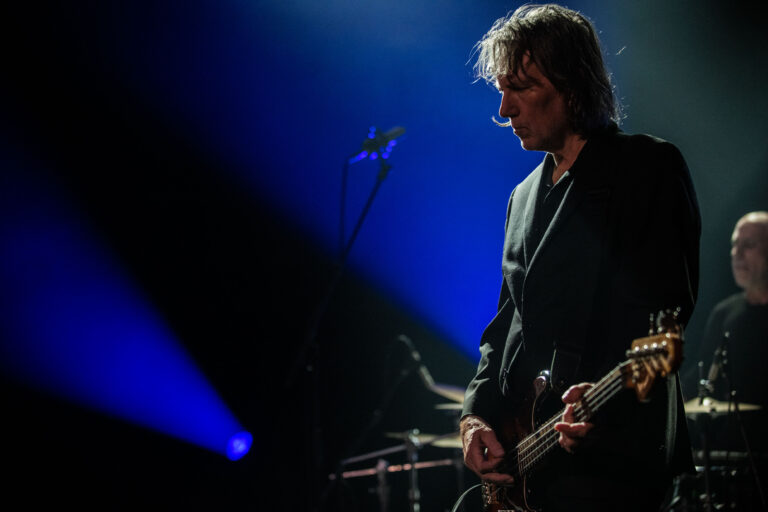Een muzikant speelt basgitaar op een podium met dramatische belichting.