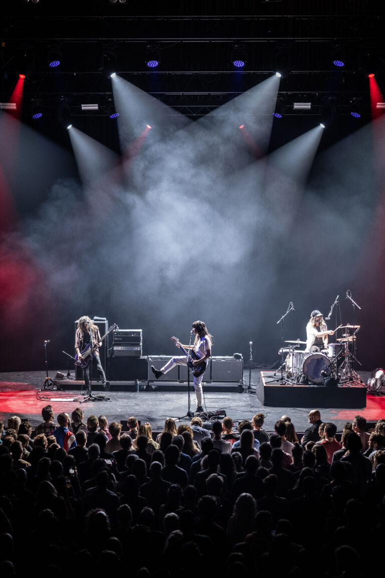 Een band speelt op een podium met kleurrijke lichten en een publiek dat toekijkt.