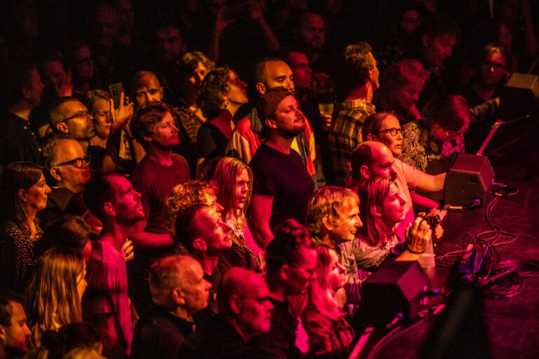 Een menigte van enthousiaste toeschouwers tijdens een optreden, verlicht door rode lichten.