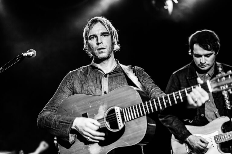 Een muzikant met een gitaar staat op het podium in zwart-wit.